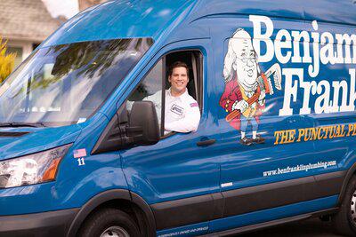 A friendly Benjamin Franklin plumber driving a service van
